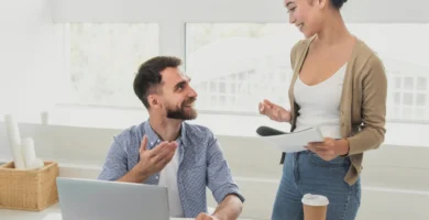 Un hombre sentado en un escritorio frente a una computadora portátil tiene una conversación con una mujer