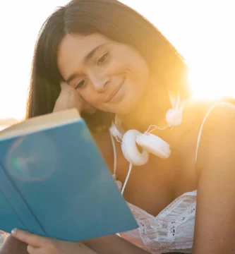 Mujer en la playa, usando auriculares y leyendo un libro, sumergida en un momento de tranquilidad junto al mar.