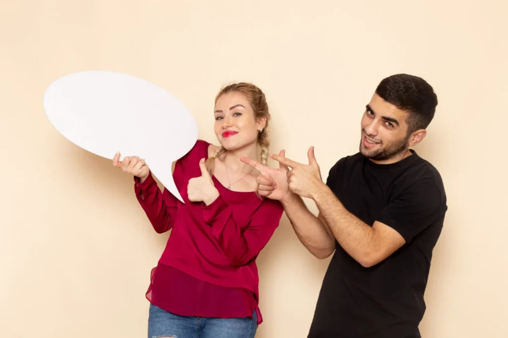 10 Consejos para Iniciar una Conversación con Confianza 2 Una mujer con una camisa roja sostiene un bocadillo en blanco mientras levanta el pulgar. Un hombre a su lado con una camisa negra hace gestos con el dedo.